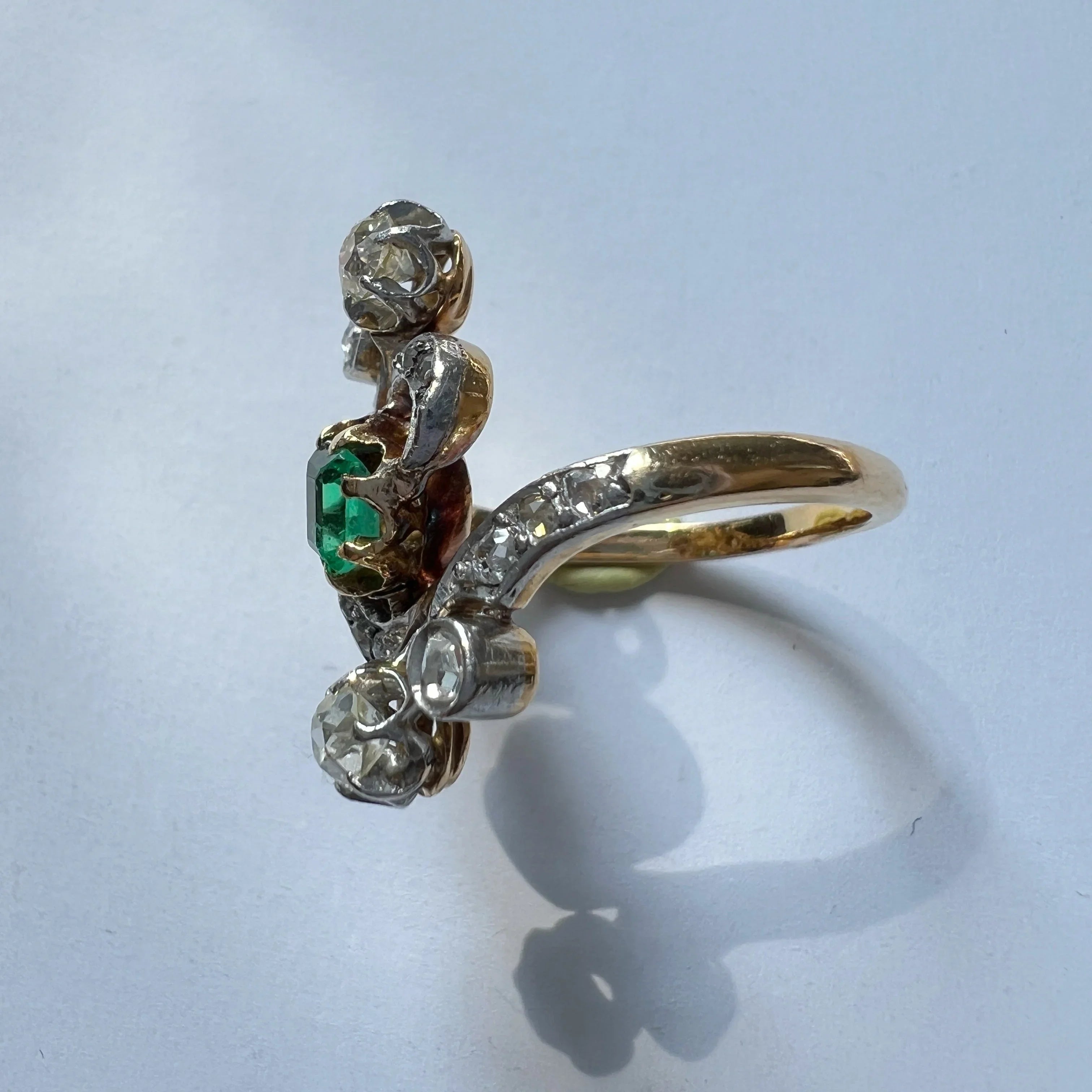 Gold ring with emerald and diamonds on a light blue background