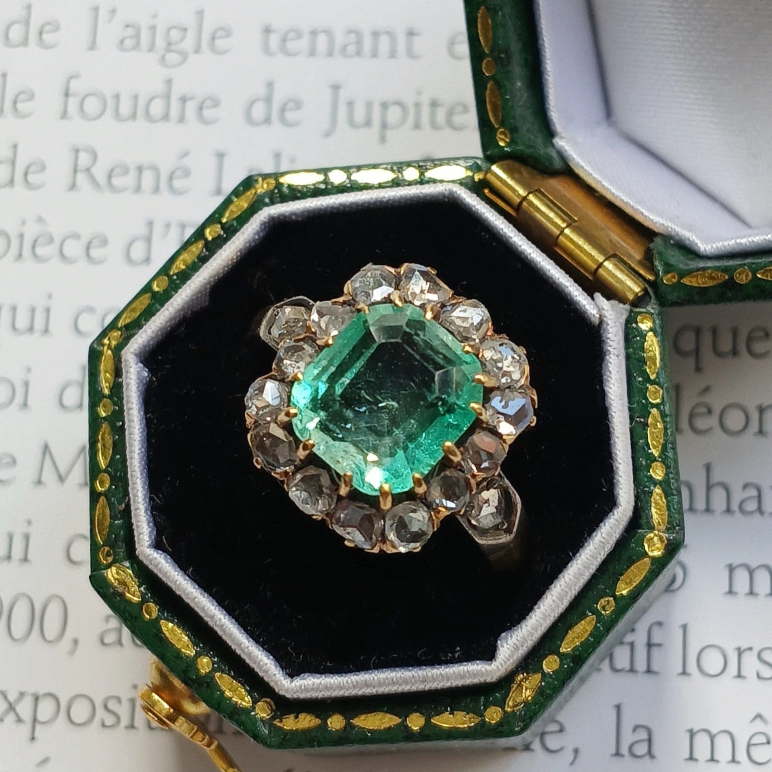 Ring with emerald and diamonds in a green and gold hexagonal box on text background